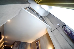 Un intérieur moderne avec un escalier menant à un niveau supérieur, un mur orné d’un motif et un objet suspendu.