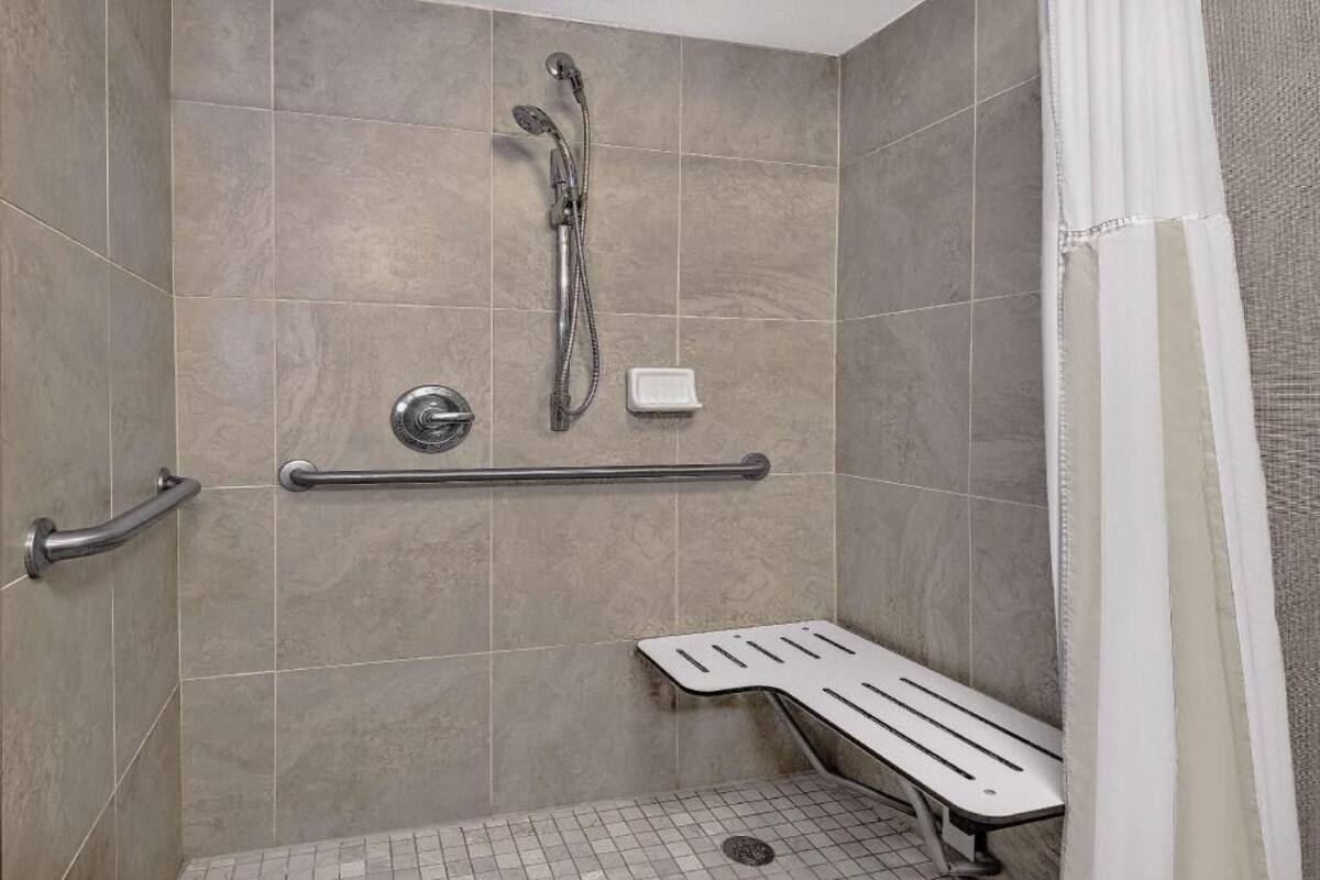 A shower with a handheld showerhead, a handheld showerhead, a grab bar, and a bench.