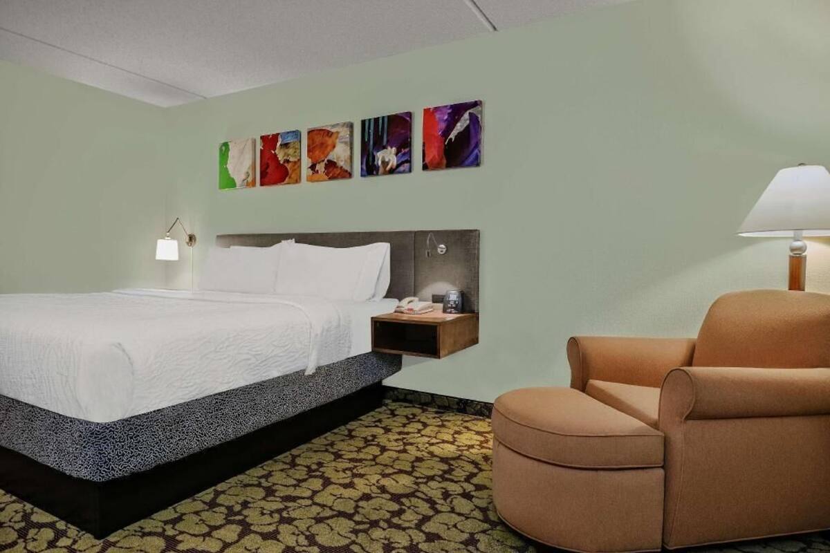Une chambre d’hôtel avec un lit, une table de chevet, une chaise et des œuvres d’art accrochées au mur.
