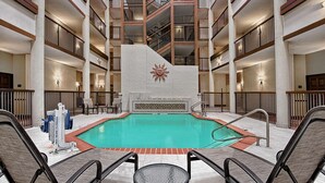 Ein Hotel-Atrium mit einem zentralen Schwimmbecken, mehreren Balkonen und einem Sonnensymbol an der Wand.