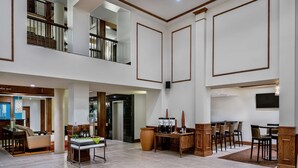 Eine großzügige Hotelhalle mit hoher Decke, einem Essbereich und einer Treppe, die in einen oberen Bereich führt.