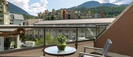 Une terrasse sur le toit, avec une table et des chaises, un pot de fleurs et une vue sur une montagne et des bâtiments en arrière-plan.