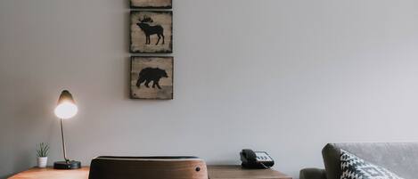A wooden desk with a lamp, a chair, a phone, and a wall-mounted animal silhouette artwork.