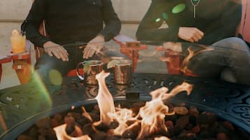 Two people sitting at a table with a glass top, a fire pit in the center, and a drink on the table.