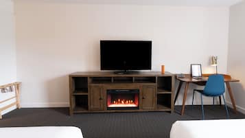 Quarto de hotel com televisão, lareira, escrivaninha e duas camas.