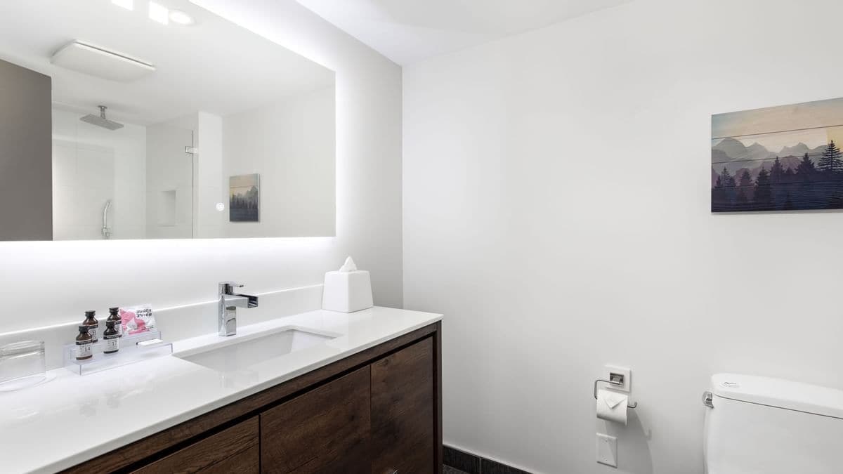 Une salle de bain moderne avec un grand miroir, deux lavabos, des toilettes et un tableau accroché au mur.