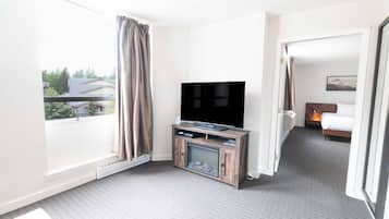A hotel room with a large flat-screen TV on a wooden stand, a bed with a headboard, and a window with curtains.