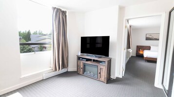 A hotel room with a large flat-screen TV on a wooden stand, a bed with a headboard, and a window with curtains.