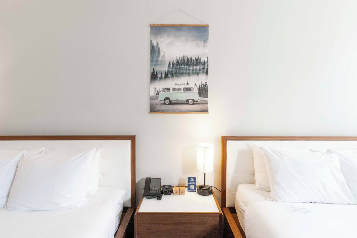 A hotel room with two beds, a nightstand with a lamp, a phone, and a sign indicating a minibar.