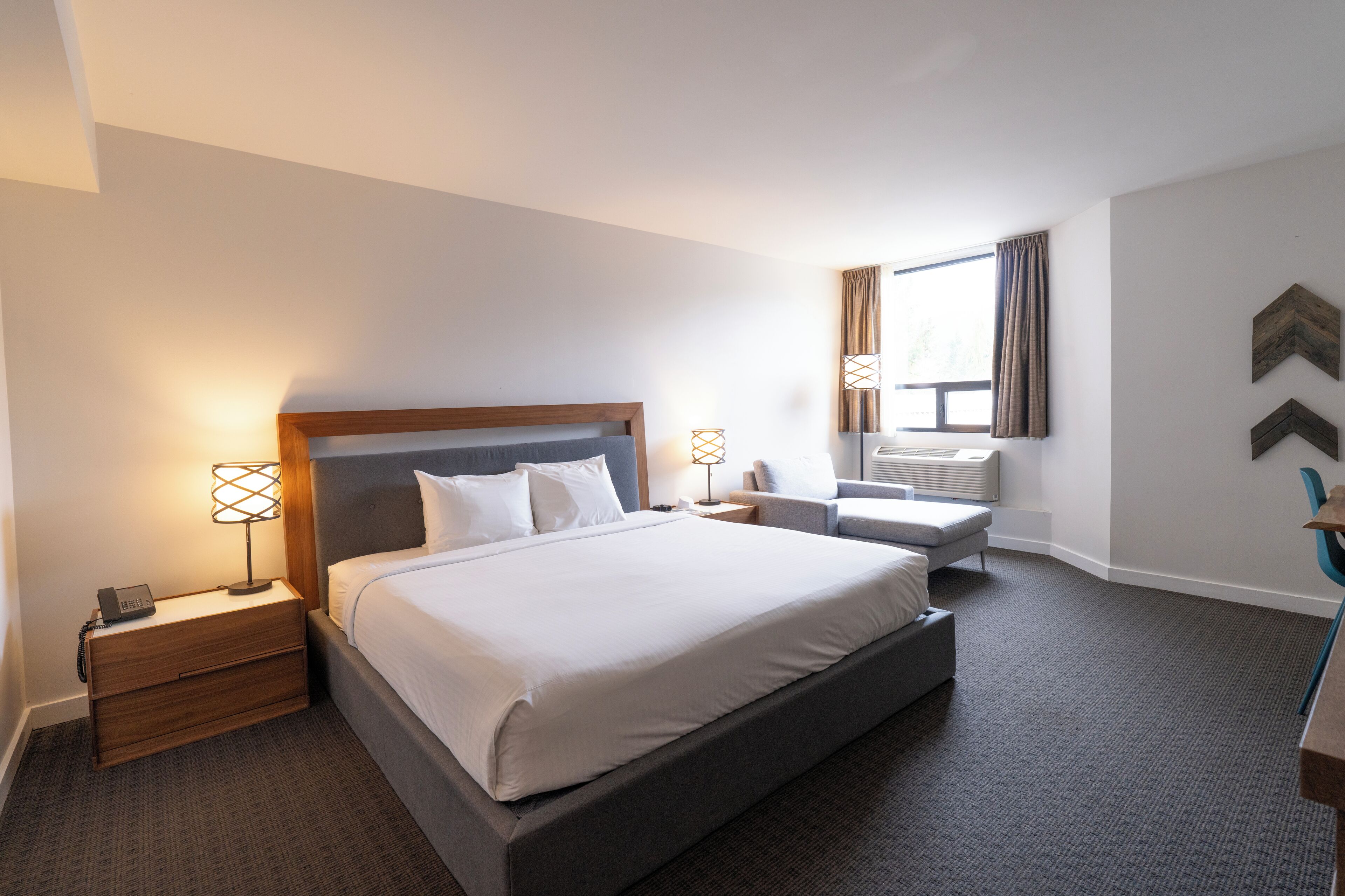 Een hotelkamer met een groot bed, nachtkastjes, een bureau, een stoel en een raam met gordijnen.