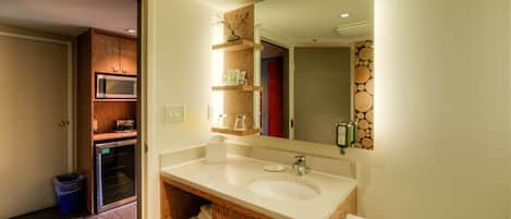 A bathroom with a wooden vanity, a sink, a mirror, and a microwave.
