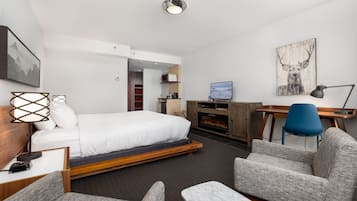 A modern hotel room with a bed, a desk, a chair, a TV, and a fireplace.