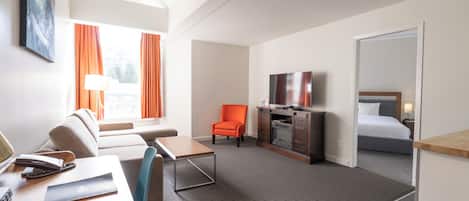 Una habitación de hotel con sofá, sillón, escritorio, televisión y cama.