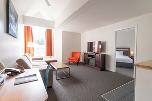 Una habitación de hotel con sofá, sillón, escritorio, televisión y cama.