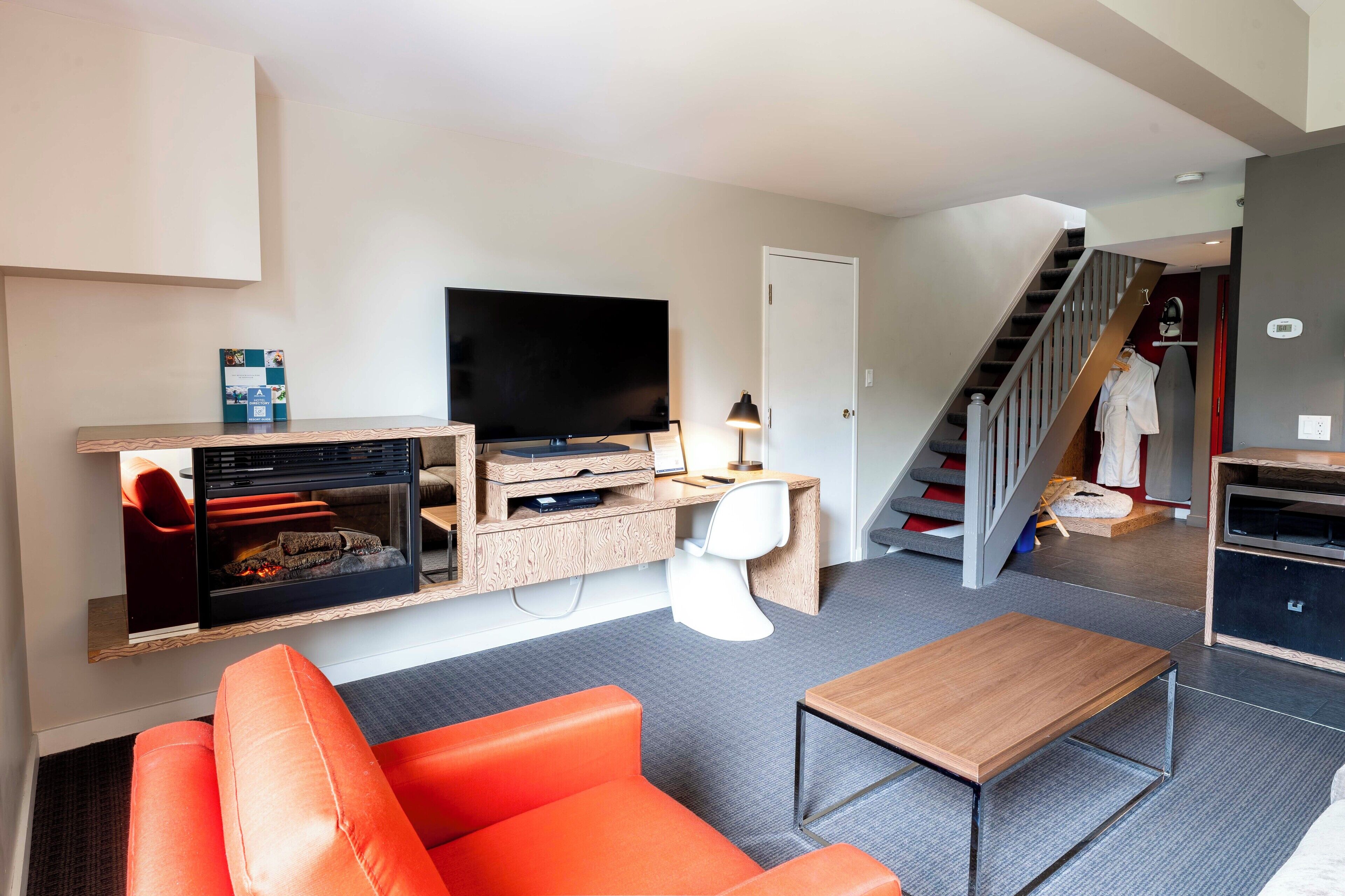 Un salon moderne avec un téléviseur à écran plat, un canapé orange, une table basse en bois et une cheminée.