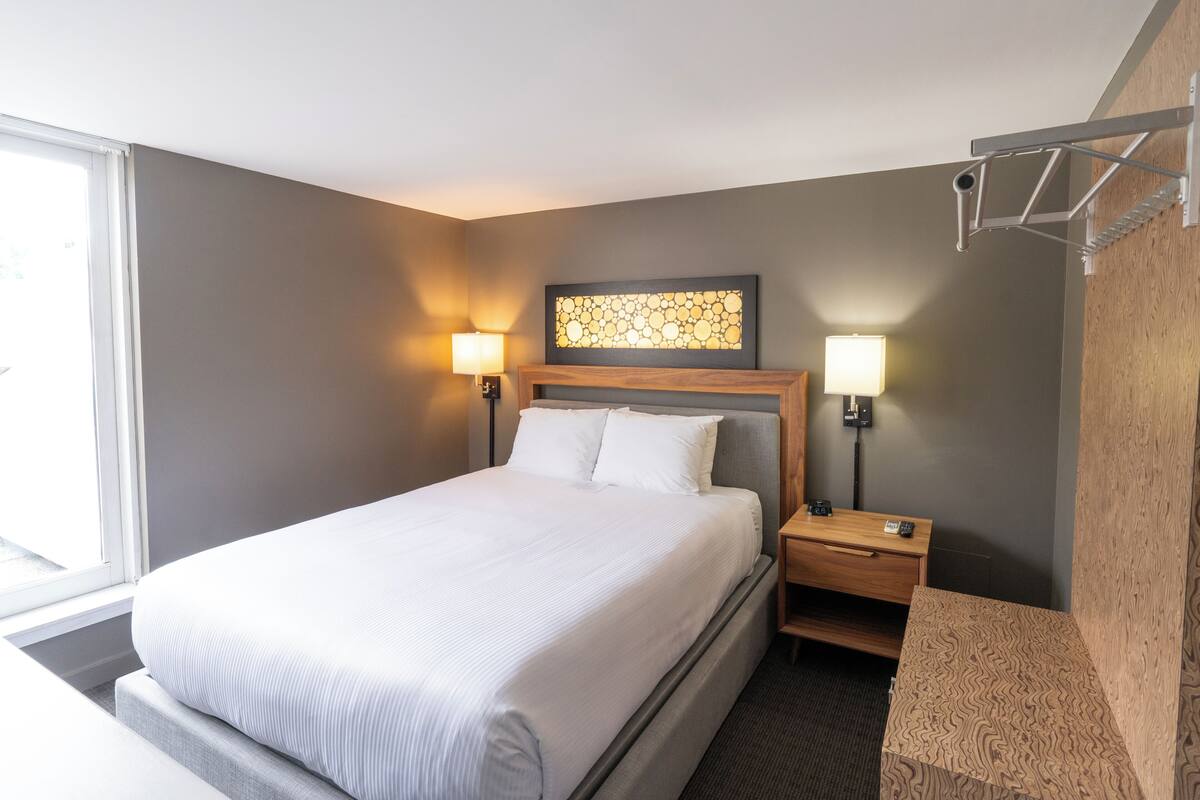 A hotel room with a large bed, two bedside lamps, a wooden headboard, a small wooden nightstand, and a wall-mounted towel rack.