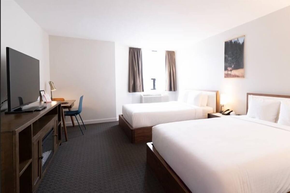 A hotel room with a bed, a desk with a computer, a chair, and a television.