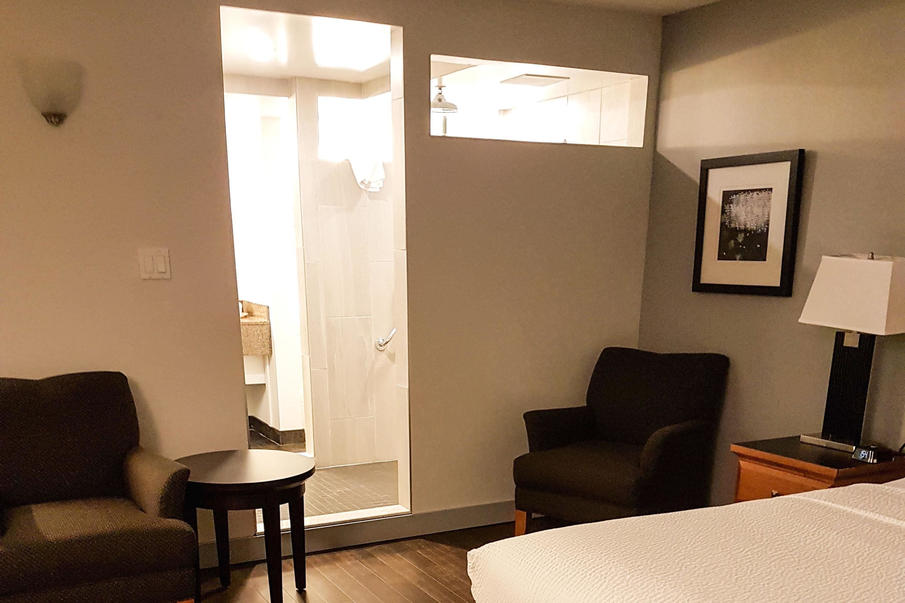 A hotel room with a bed, two armchairs, a small table, a lamp, and a framed picture on the wall.
