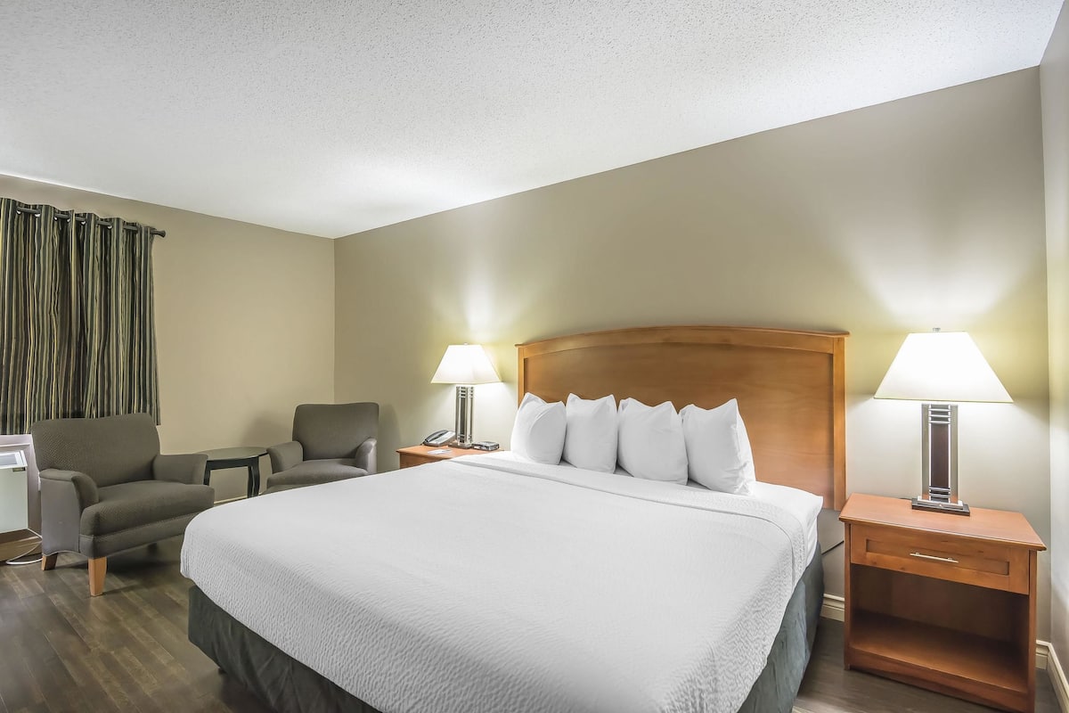 A hotel room with a large bed, two armchairs, a desk, and two bedside lamps.