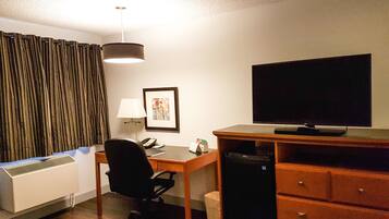Una habitación de hotel con escritorio, silla, televisor y un pequeño bote de basura.