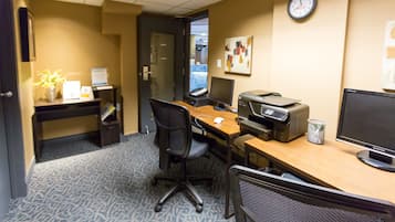 A hotel office with a desk, computer, printer, and a clock on the wall.