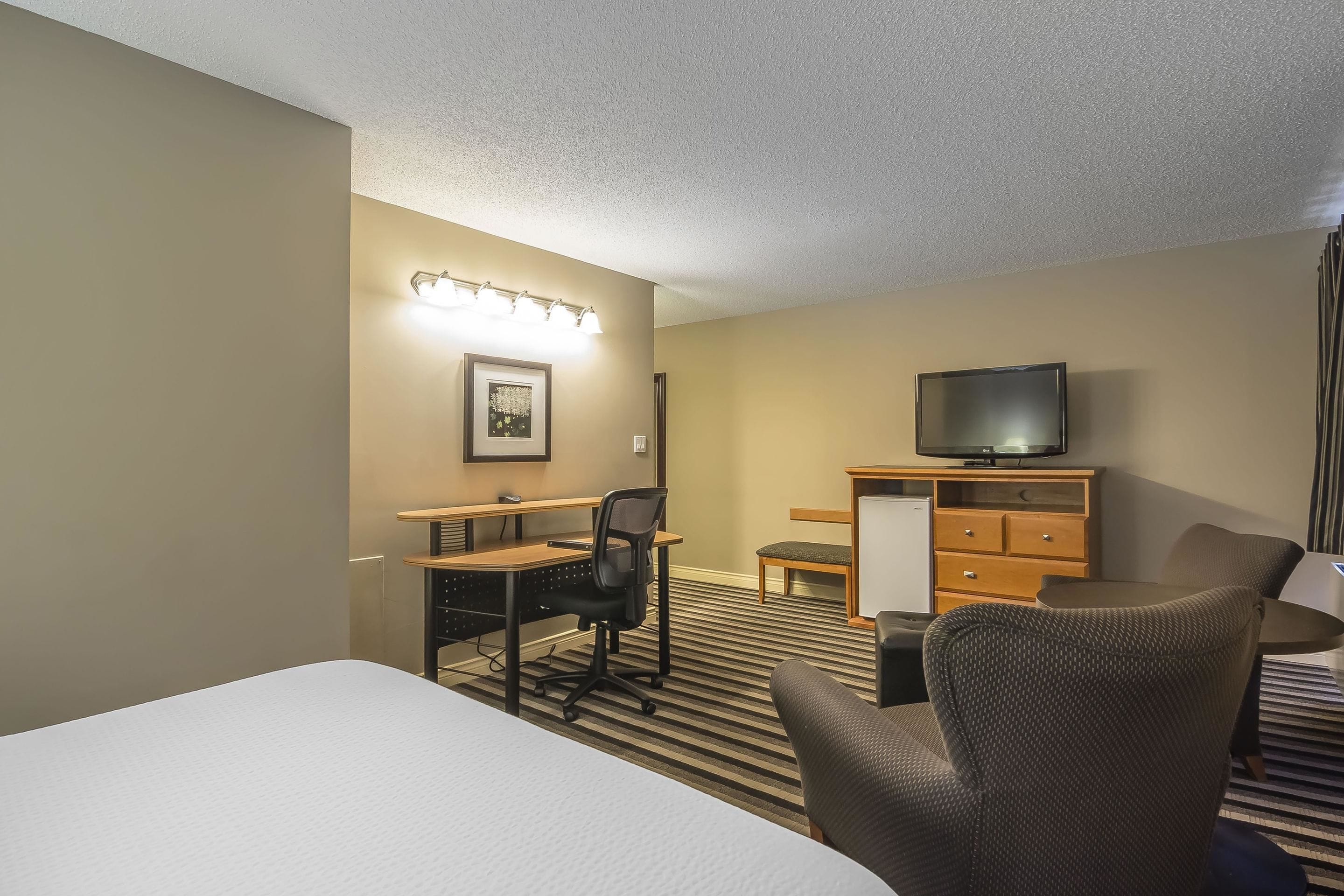 A hotel room with a bed, a desk with a chair, a television, and a dresser.