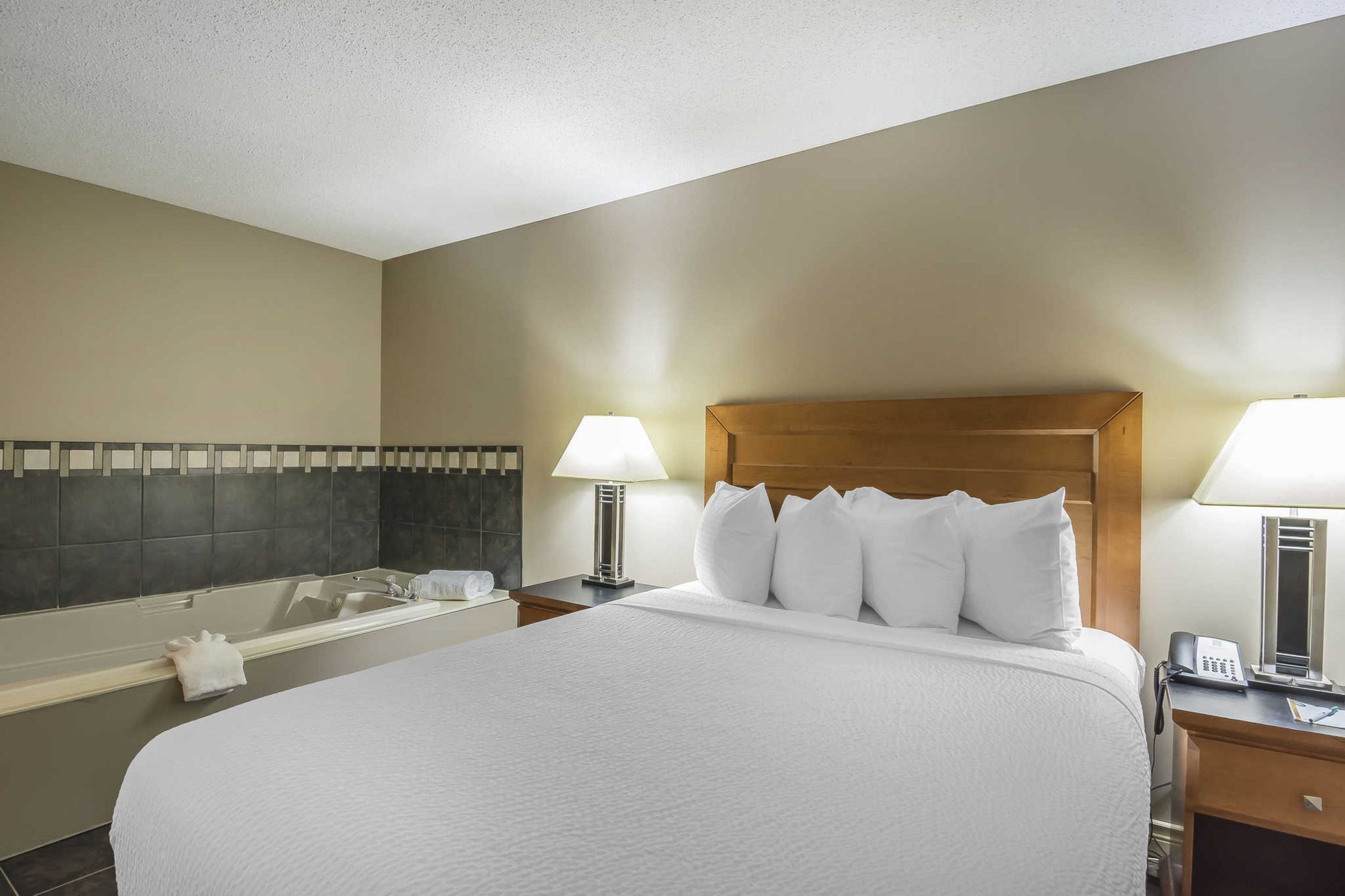 A hotel room with a large bed, a bathtub, and two bedside lamps.