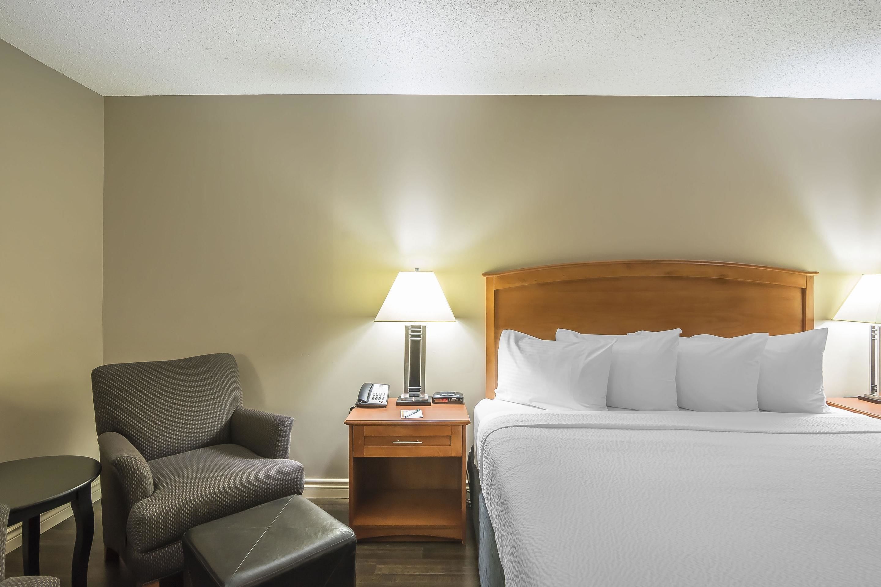 A hotel room with a bed, a chair, a nightstand with a lamp, and a small table.