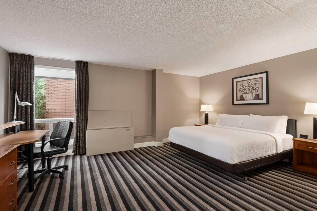 Ein Hotelzimmer mit Bett, Schreibtisch, Stuhl und Blick auf ein Backsteingebäude.