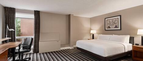 Una camera d'albergo con un letto, una scrivania, una sedia e vista su un edificio in mattoni.