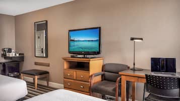 Habitación de hotel con cama, escritorio con laptop, televisor, silla, lámpara de escritorio y una mesita con cafetera.