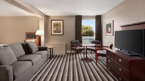 A hotel room with a sofa, a small table, two chairs, a TV, and a window with a view. - Royal Hotel Regina, Trademark Collection by Wyndham (Regina)