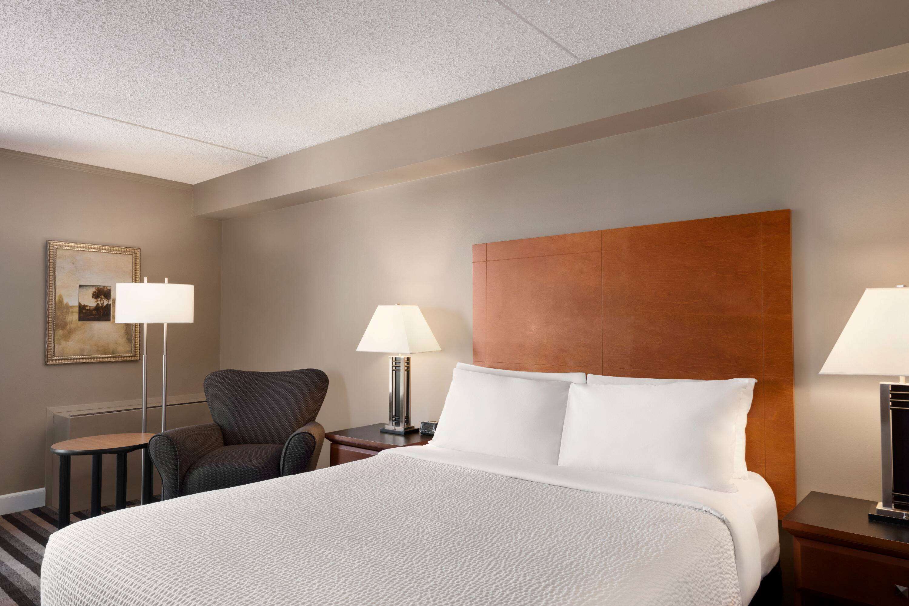 Ein Hotelzimmer mit einem großen Bett, zwei Nachttischen mit Lampen, einem Sessel und einem gerahmten Bild an der Wand.