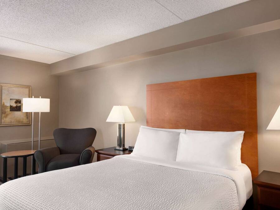 Ein Hotelzimmer mit einem großen Bett, zwei Nachttischen mit Lampen, einem Sessel und einem gerahmten Bild an der Wand.