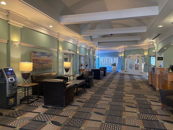 A hotel lobby with a patterned carpet, leather seating, an ATM, and a reception desk.