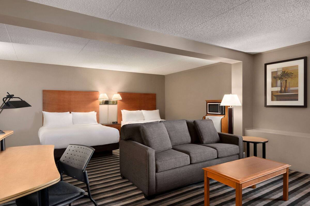 Ein Hotelzimmer mit Bett, einer Couch, einem Schreibtisch, einem Sessel, einer Lampe und einem Bild an der Wand.