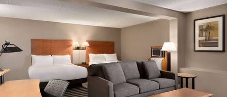 A hotel room with a bed, a sofa, a desk, a chair, a lamp, and a picture on the wall.