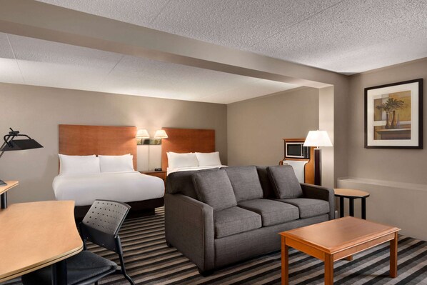 A hotel room with a bed, a sofa, a desk, a chair, a lamp, and a picture on the wall.