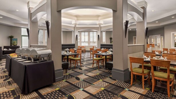 A spacious dining area with multiple tables and chairs, a buffet setup, and a patterned carpet. - Royal Hotel Regina, Trademark Collection by Wyndham (Regina)