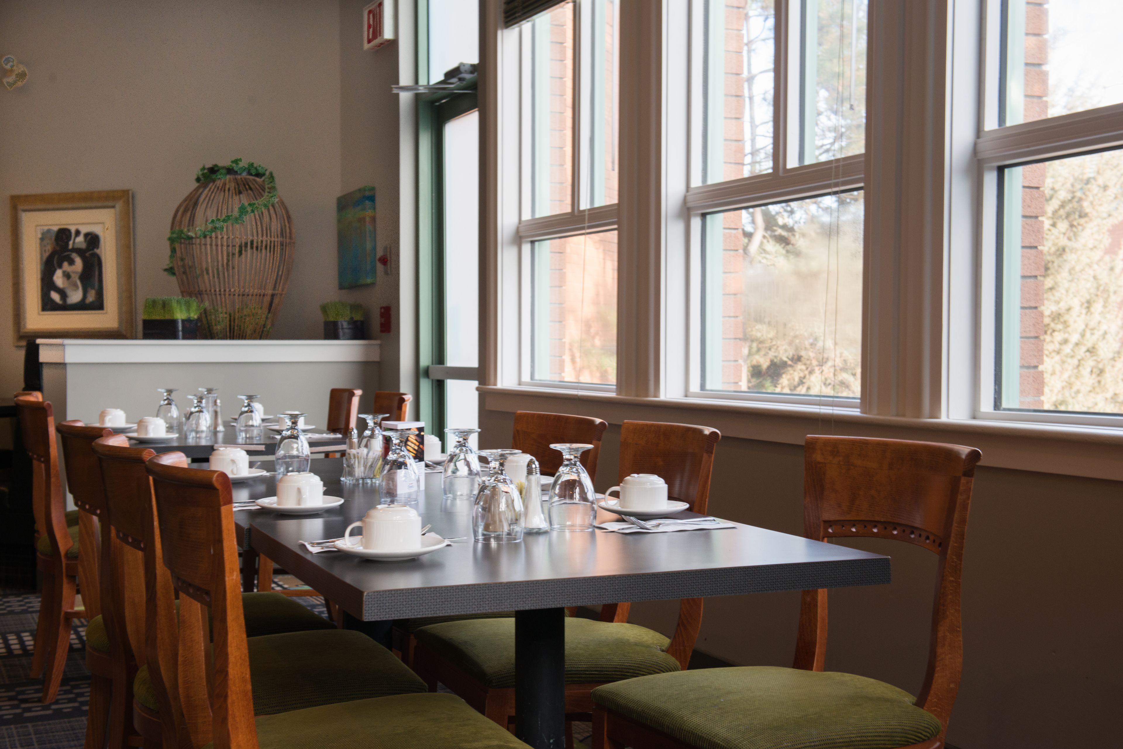 A dining area with a long table set for four, surrounded by wooden chairs with green cushions.