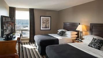 Ein Hotelzimmer mit zwei Betten, einem Schreibtisch mit Fernseher, einem gerahmten Bild an der Wand und einem Vorhangfenster.