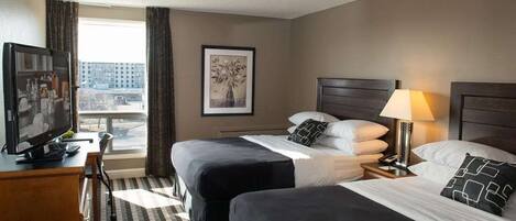 Habitación de hotel con dos camas, un escritorio con televisor, un cuadro en la pared y una ventana con cortinas.