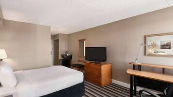 A hotel room with a bed, a TV, a desk, a chair, a dresser, and a lamp.