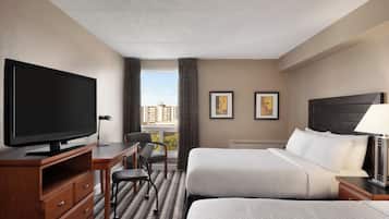 A hotel room with a television, two beds, a desk, a chair, and a window with curtains.