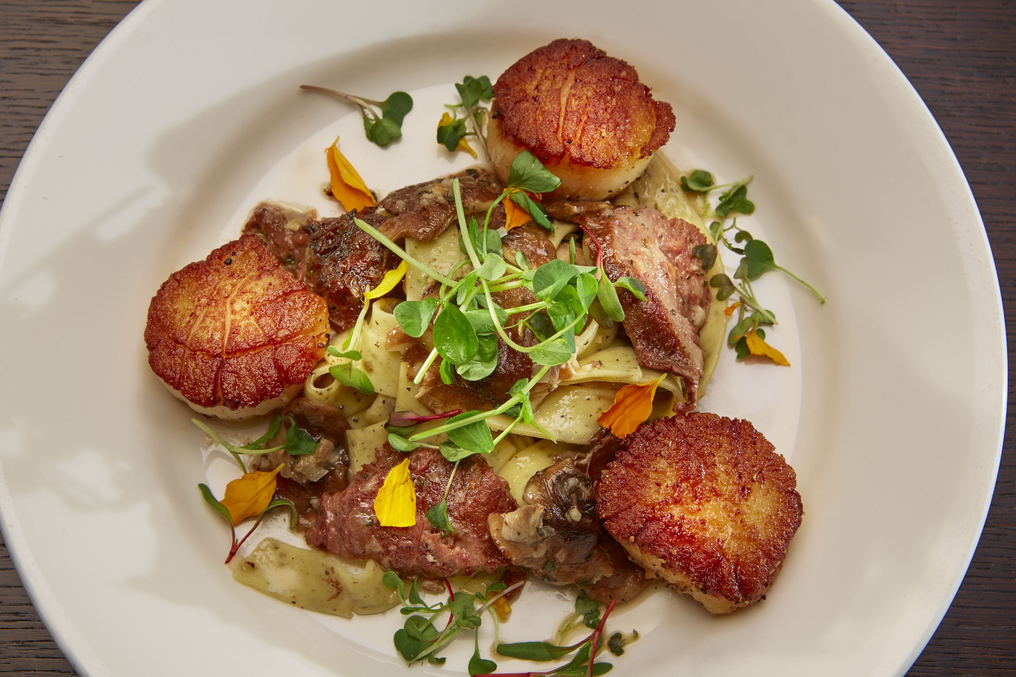 A plate of food with seared scallops, meat, and vegetables.