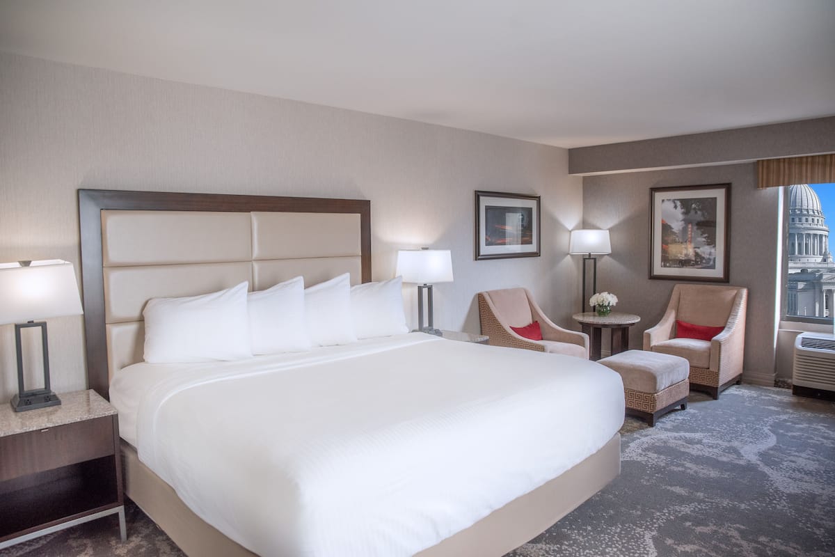Habitación de hotel con una cama grande, dos sillones, una mesita y una lámpara.