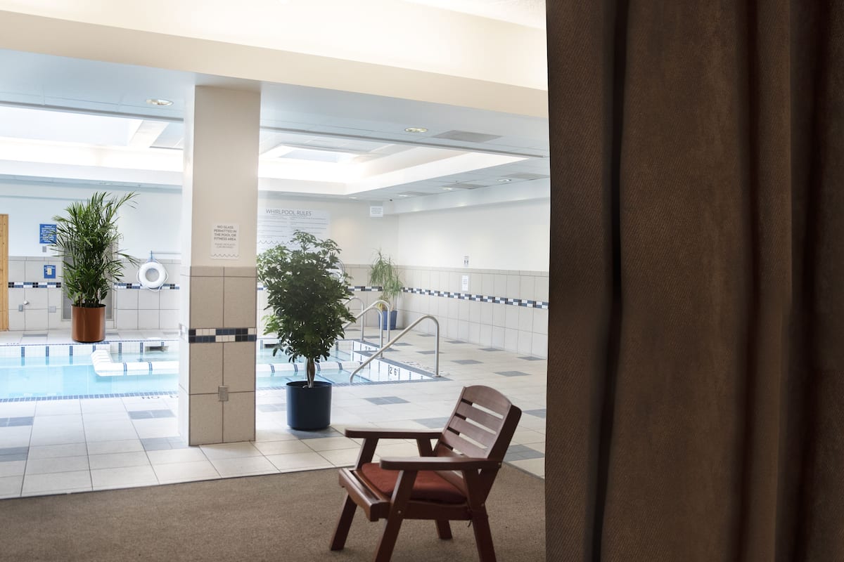 Zona de piscina con una silla y plantas en macetas, un cartel que indica que no se permite vidrio en el gimnasio, y piso de baldosas.