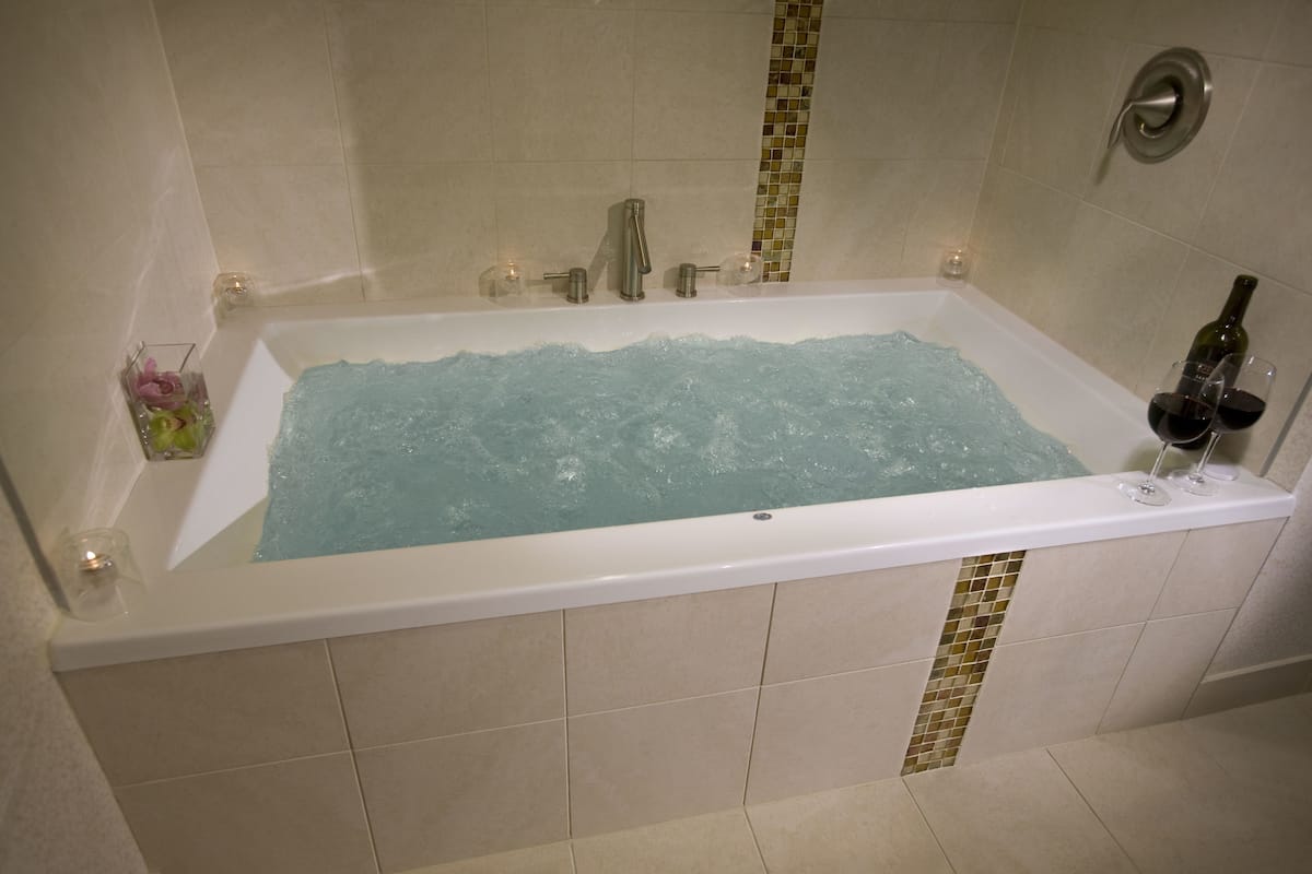 Una bañera rectangular con una copa de vino tinto y una botella en el borde.