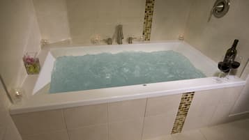 Une baignoire rectangulaire, un verre de vin rouge et une bouteille posés sur le bord.