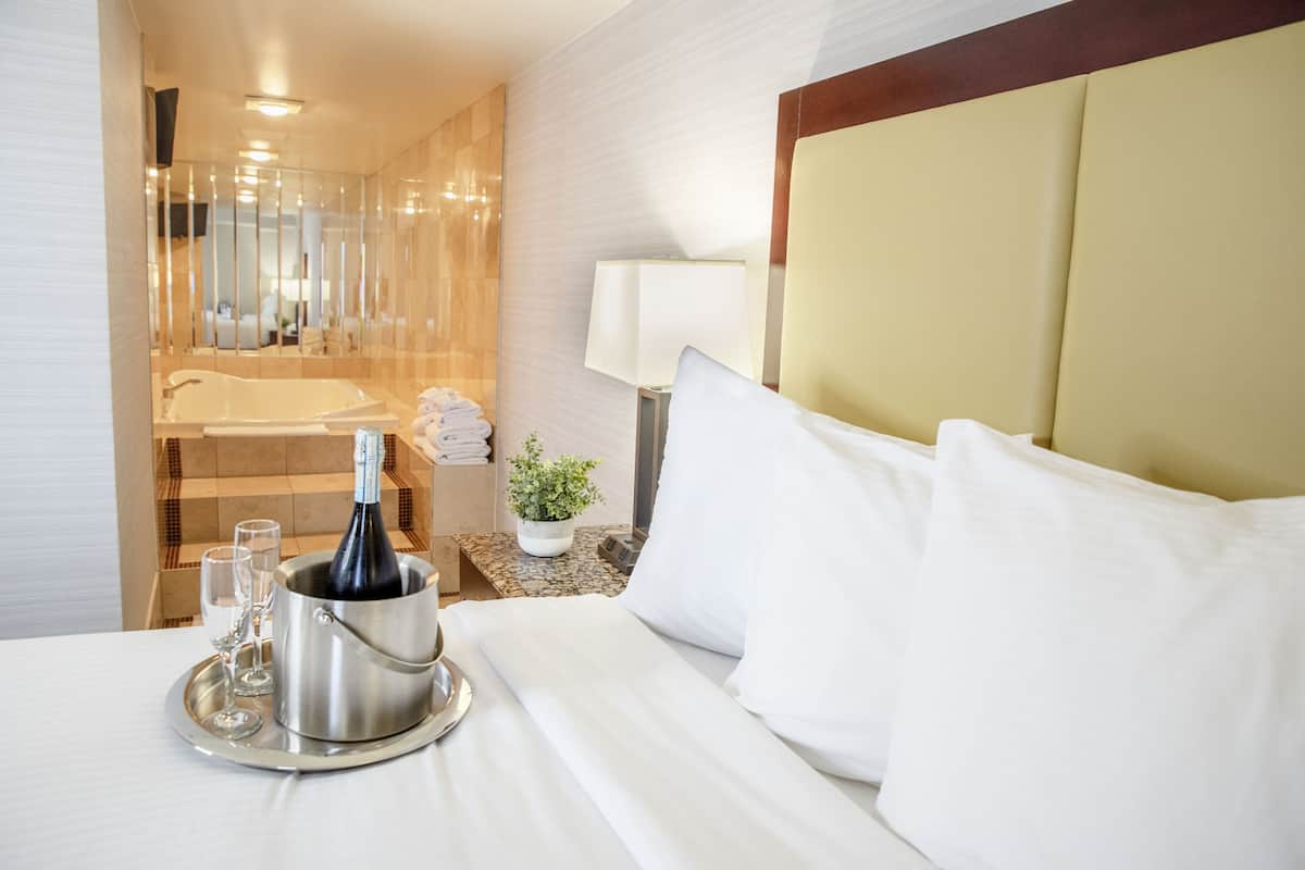 Una habitación de hotel con cama, una mesita de noche con champán, copas y una bandeja.